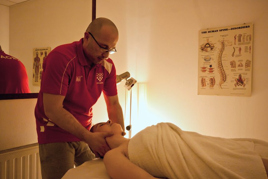 Dejan Spasić treating a client’s neck, with a spine chart in the background